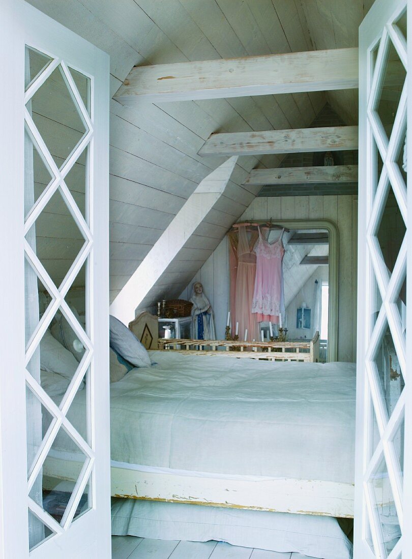 Blick durch offene Türen auf Bett in ausgebautem Dach mit holzverkleideten Wänden