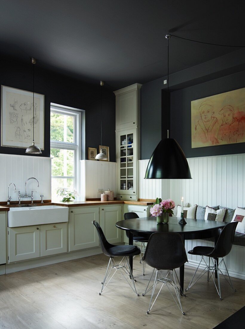 Shell chairs around a black dining table below black-painted ceiling in a rustic kitchen