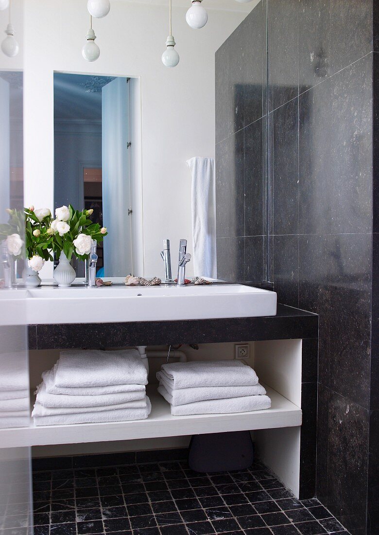 Modern washstand with towels in open-fronted shelves below next to dark marble wall