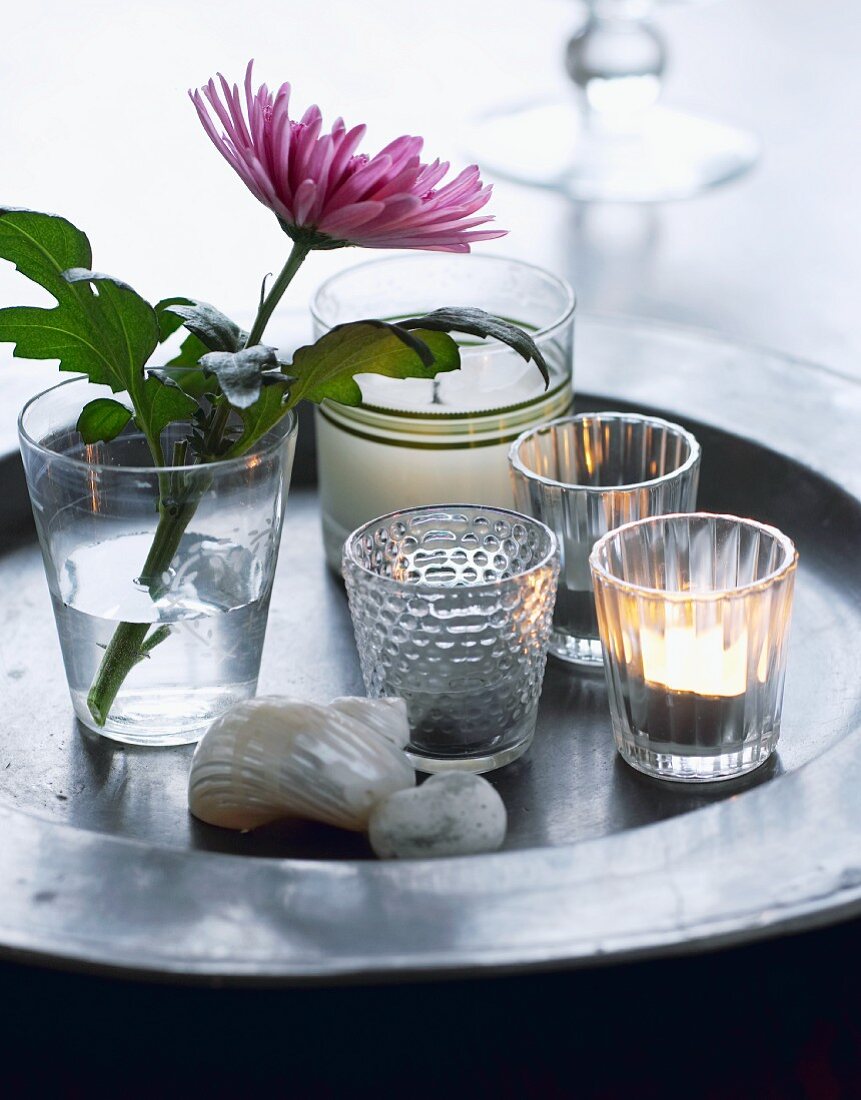 Windlichtgläser und Blume im Wasserglas auf Tablett aus Metall