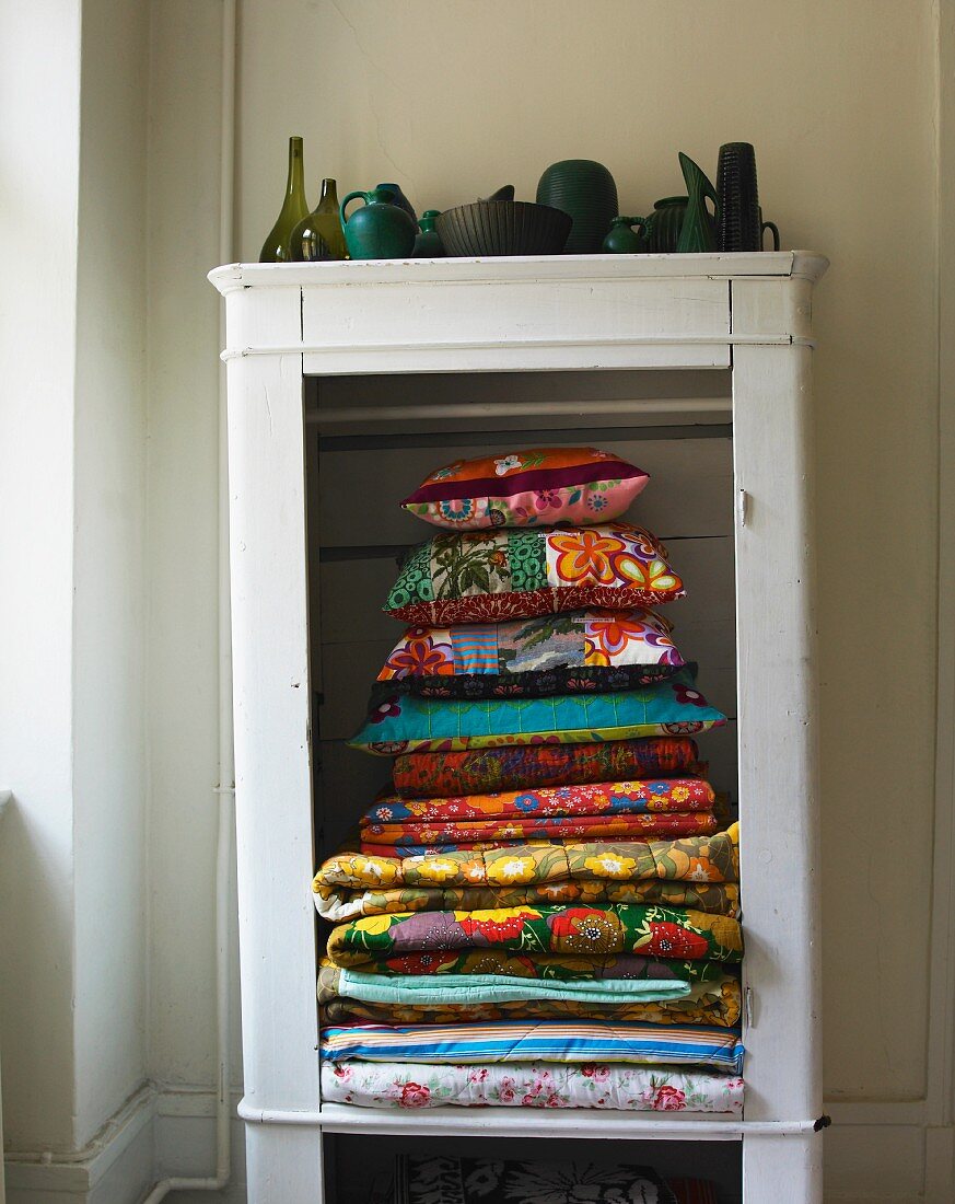 Stack of colourful blankets and cushions in open-fronted cupboard