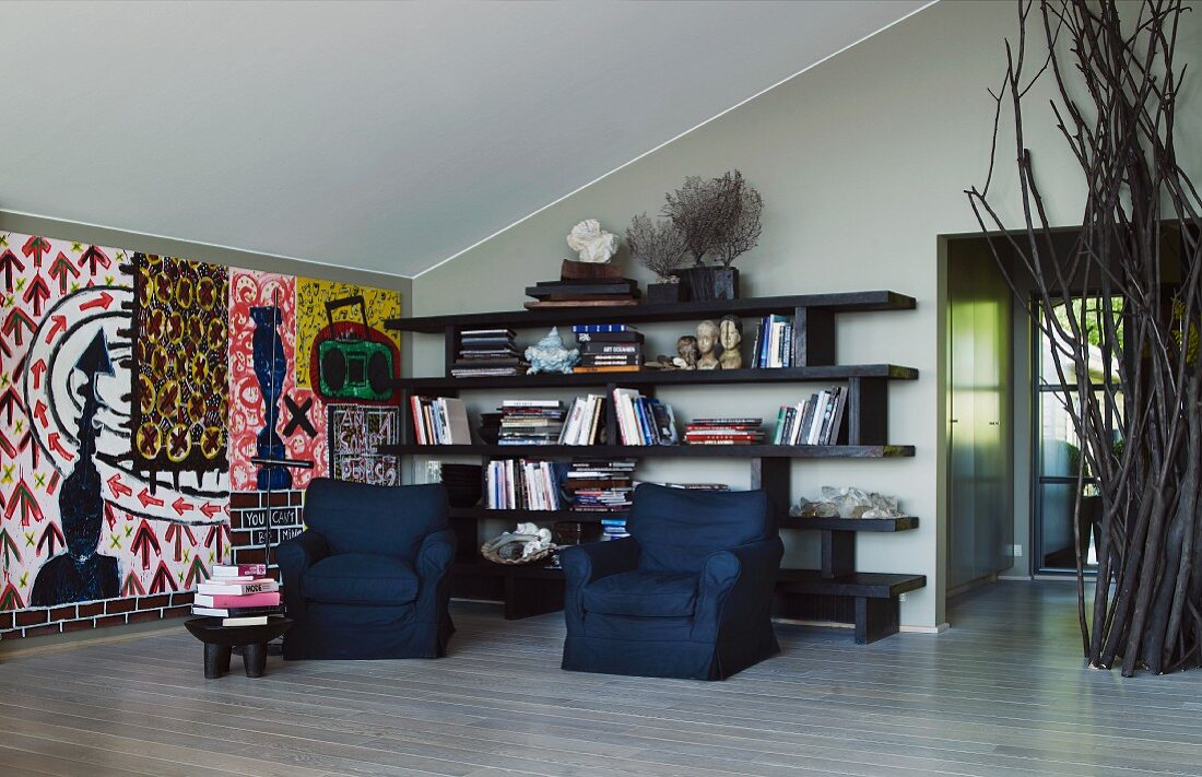 Interior with black upholstered armchairs in front of shelving and colourful painted wall