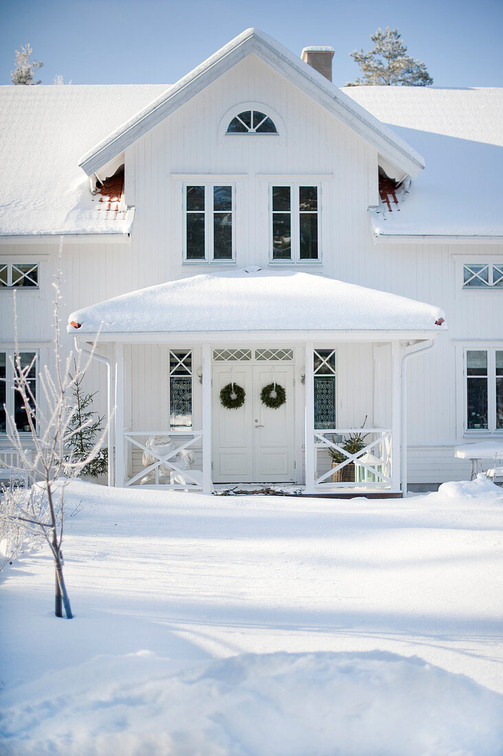 Weisses Holzhaus mit überdachtem Eingang in verschneiter Landschaft