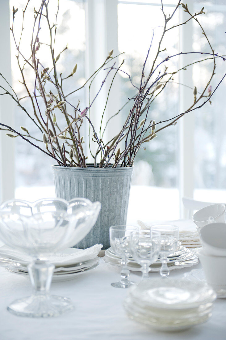 Schalen und Gläser vor Metall Vase mit Blumenzweigen auf Tisch mit Tischdecke