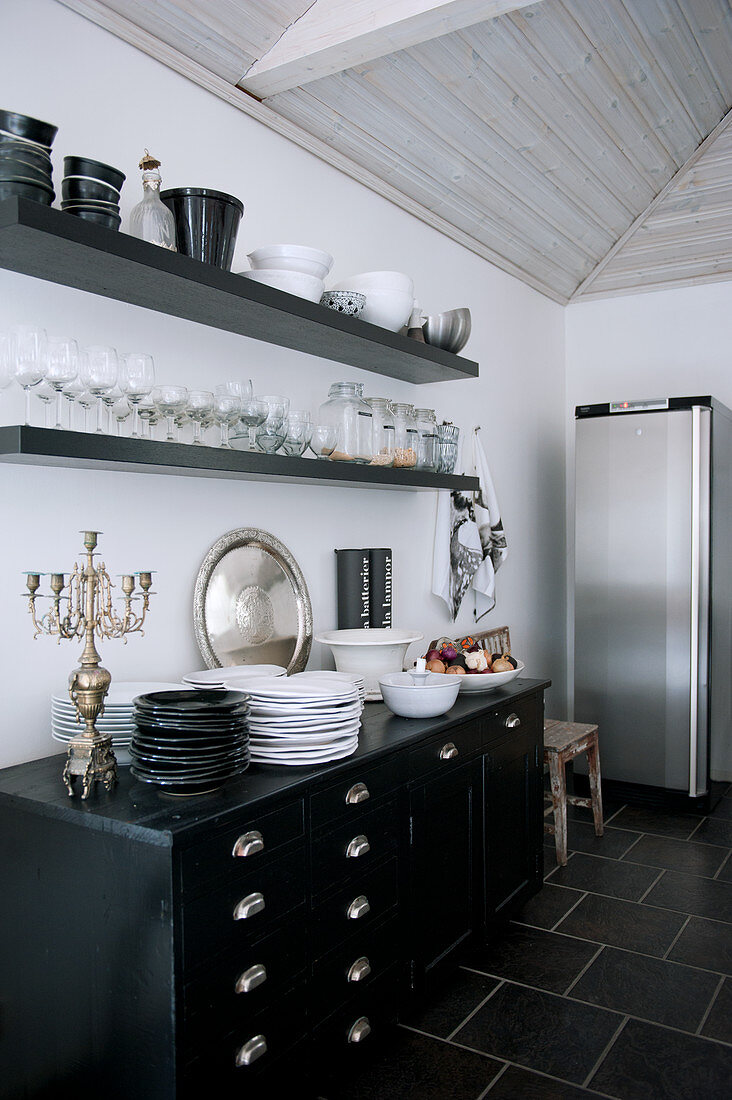 Wandborde über altem Schubladenschrank mit schwarzem und weißem Geschirr, Gläsern, silbernem Leuchter und Edelstahlkühlschrank in Loftküche