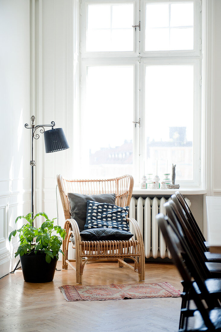 Rattanstuhl mit Kissen und Vintage Stehleuchte vor Fenster in Wohnzimmerecke mit traditionellem Flair