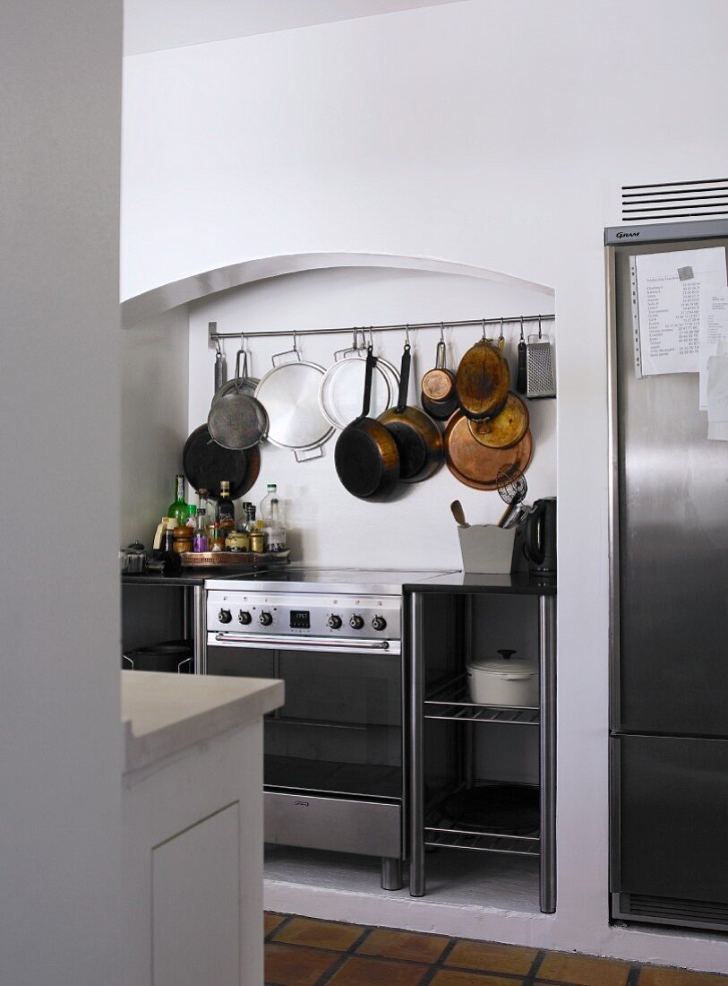 Modern cooker in niche below utensils hanging from hooks