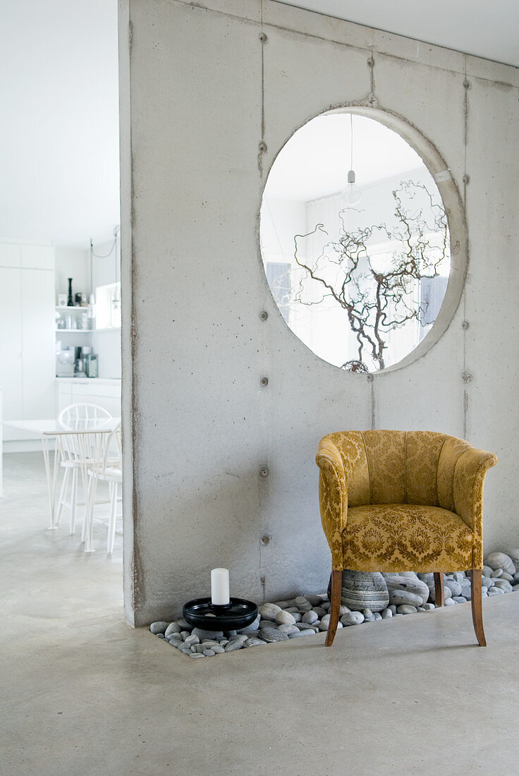 Kieselbeet im Estrichboden und Vintage Samtsessel vor einer rohen Betonwand als Raumteiler mit Durchblick
