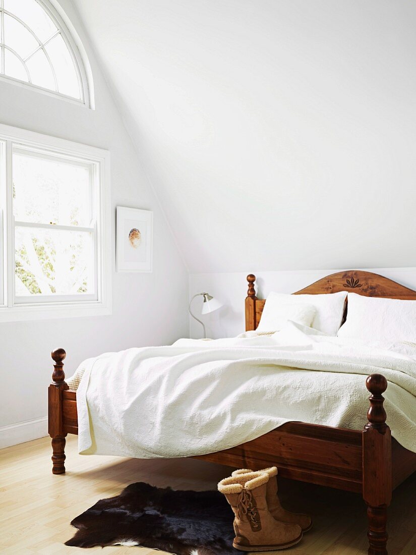 Antikes Bettgestell aus Holz und weiße Bettwäsche im Dachzimmer neben Fenster mit halbkreisförmigem Oberlicht