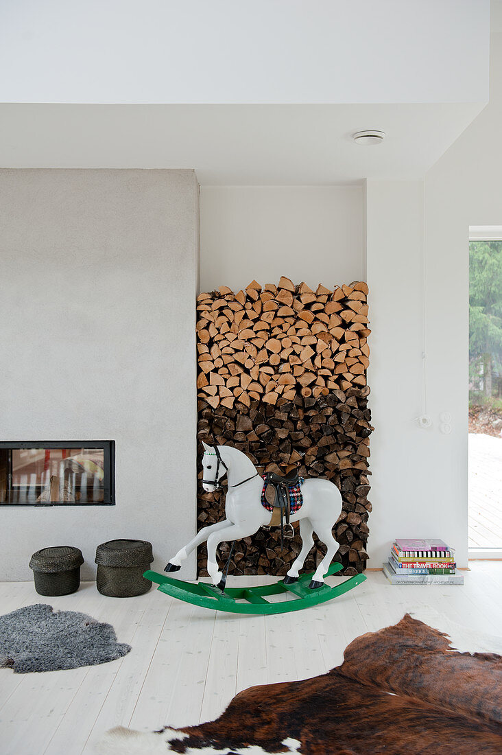 Bemaltes Schaukelpferd vor Holzstapel in Wandnische in modernem Wohnraum mit Tierfellen auf weißem Dielenboden