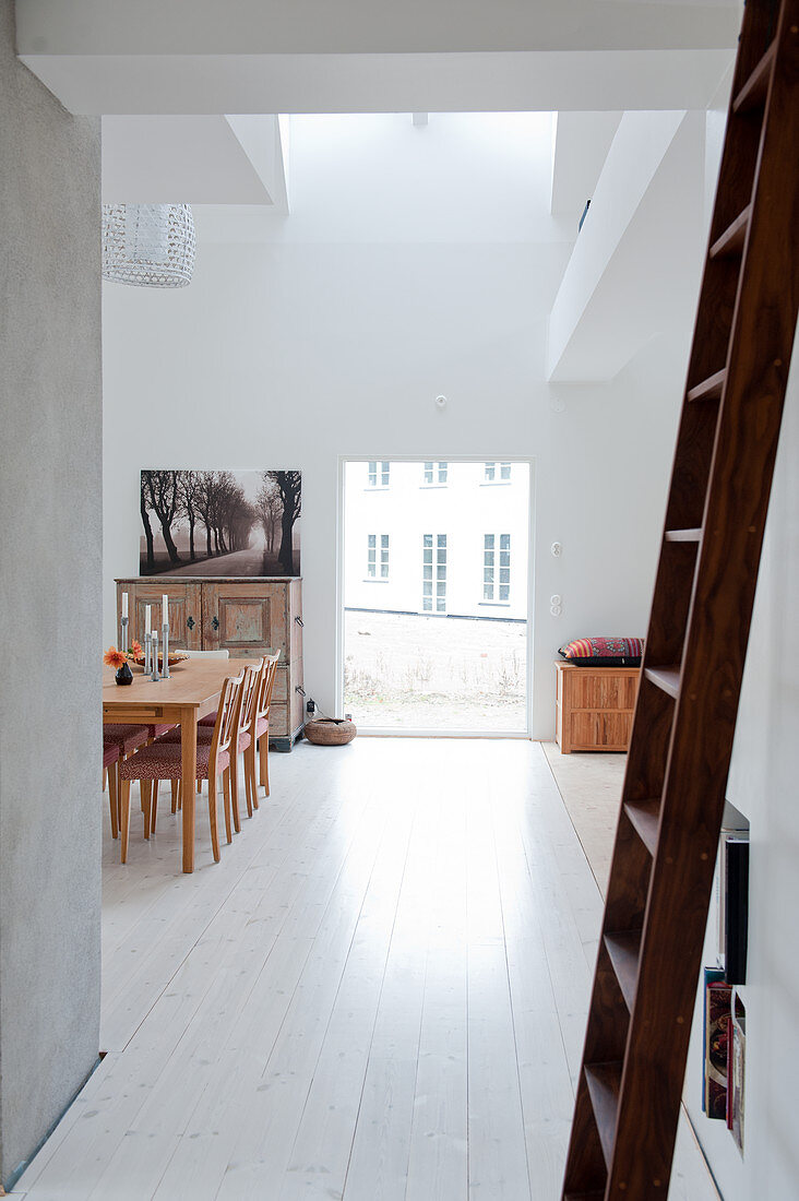 Holzleiter vor Durchgang und Blick in minimalistischen Wohnraum auf Essplatz neben raumhohem Fenster