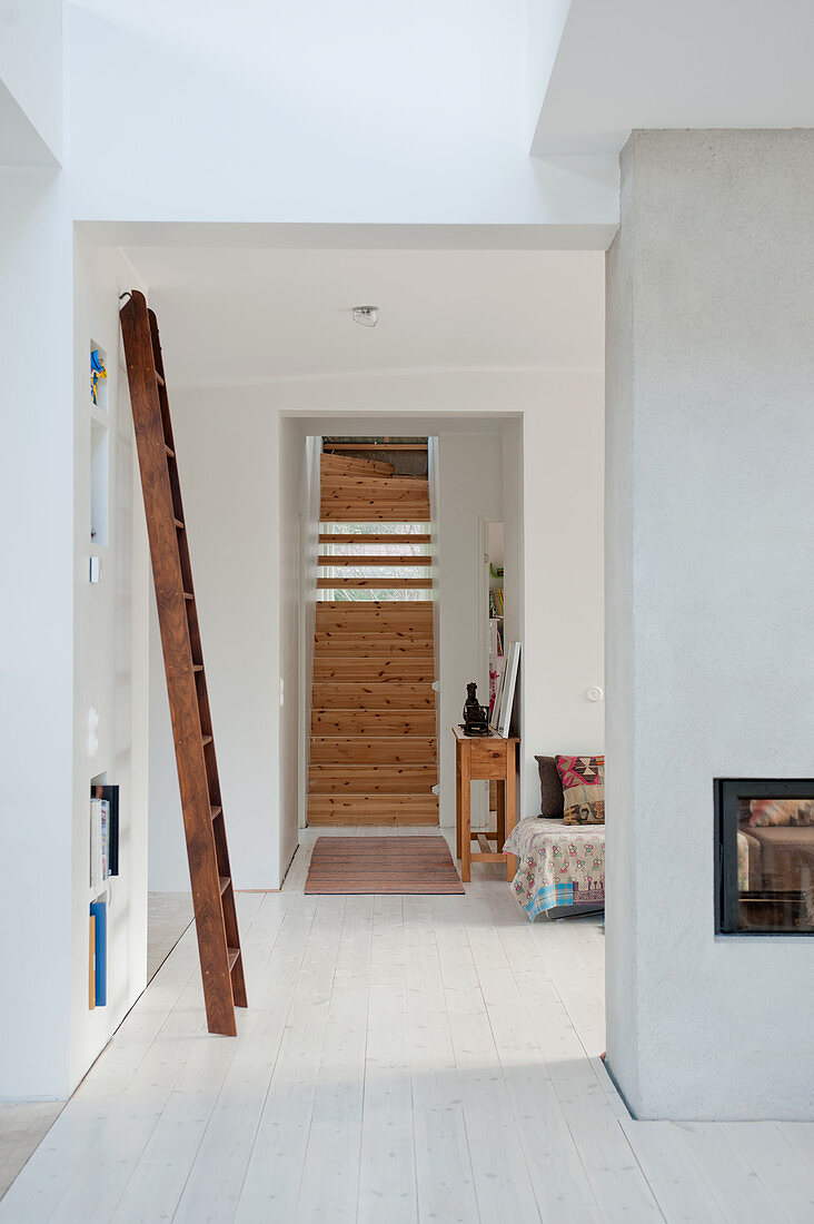 Blick durch raumhohen Durchbruch auf Holztreppe in minimalistischem Wohnraum mit weißem Dielenboden