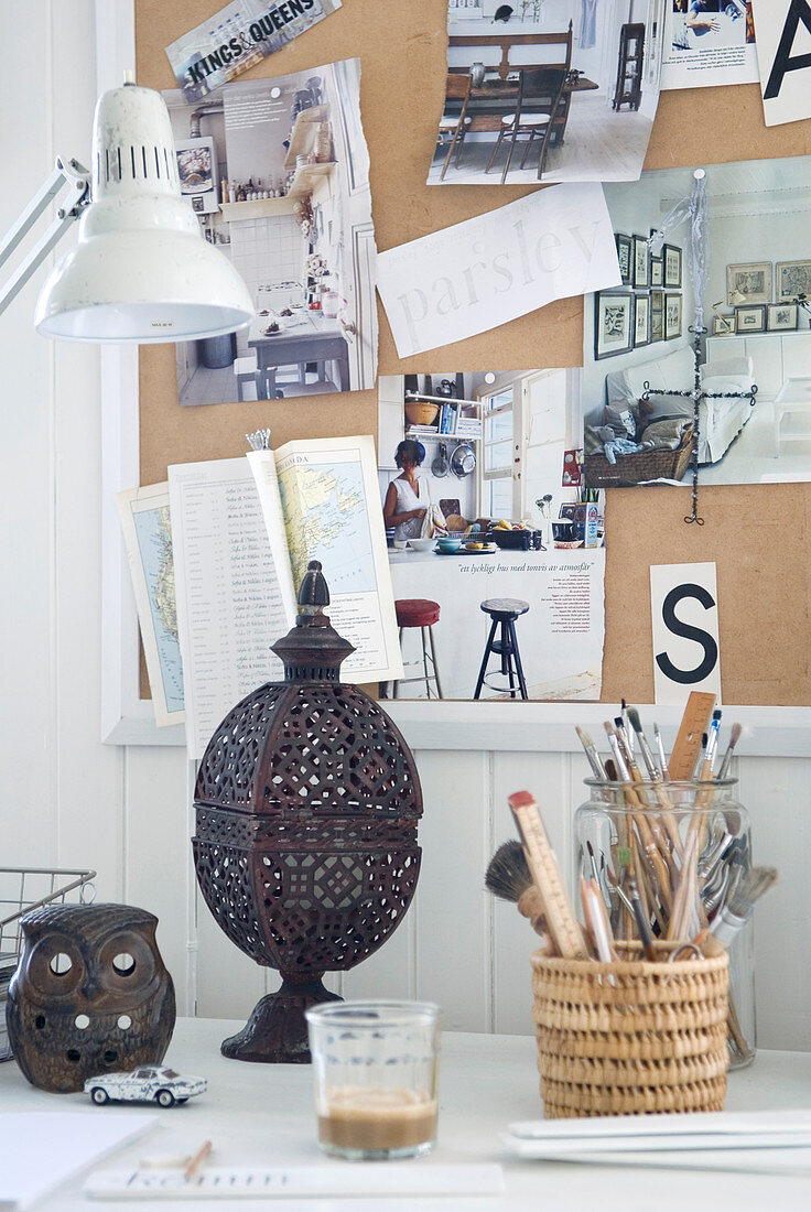Schreibtisch mit orientalischem Windlicht vor Pinnwand an weisser Holzwand