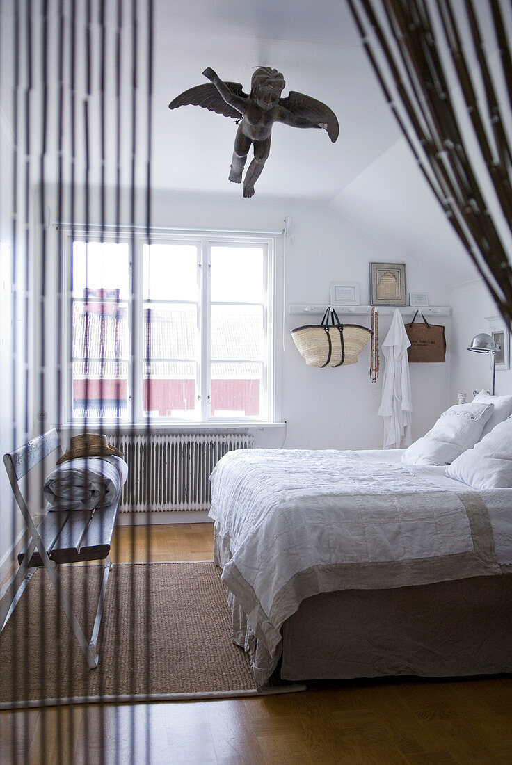 Blick durch offenem Fadenvorhang in Sschlafzimmer mit Holzbank und Engelfigur an der Decke