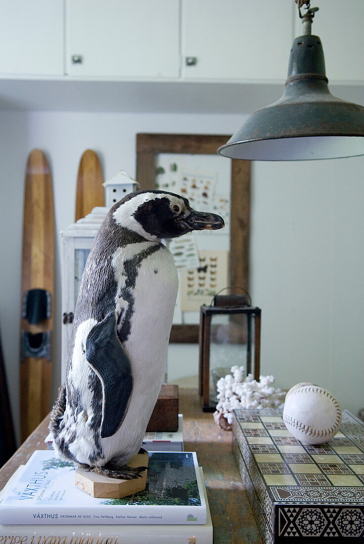 Stuffed penguin on stacked books and board game on table below vintage pendant lamp