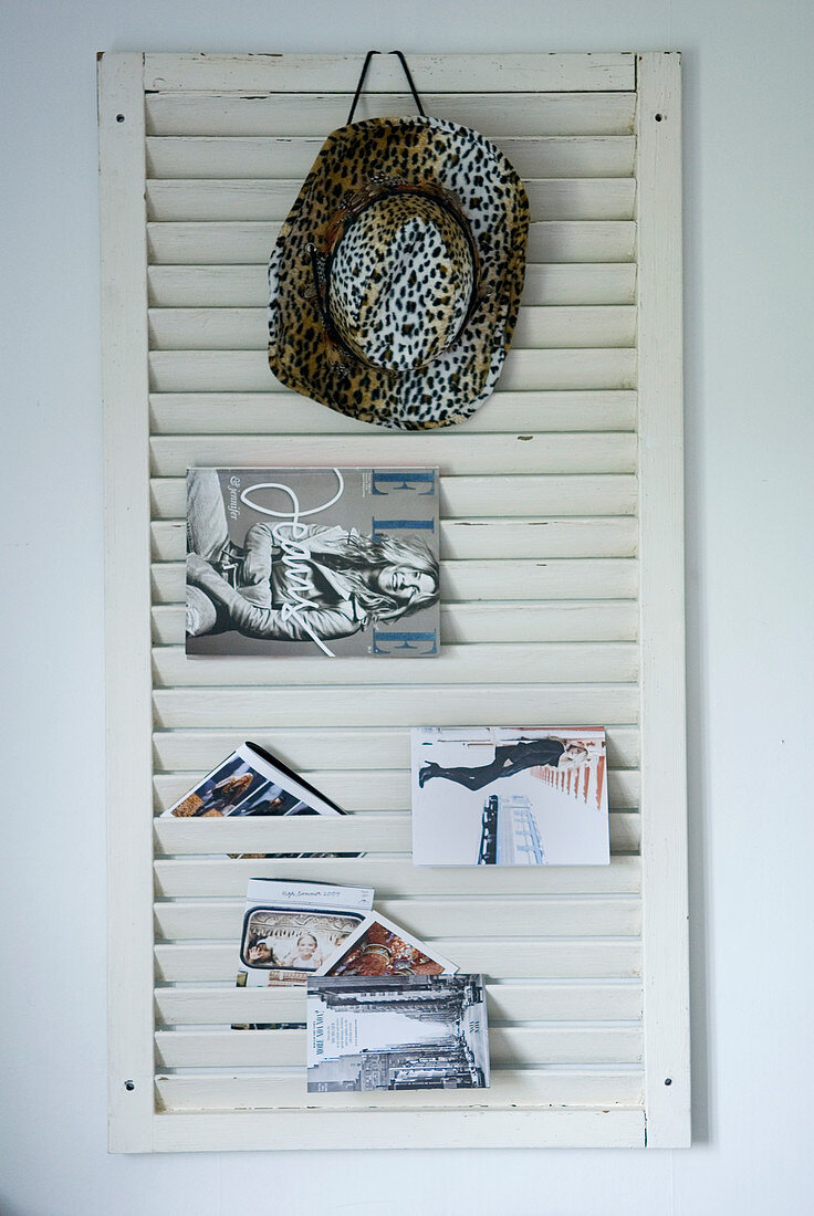 Weisser Jalousie-Fensterladen als Zeitschriftenhalter mit aufgehängtem Cowboyhut und Prospekten an Wand