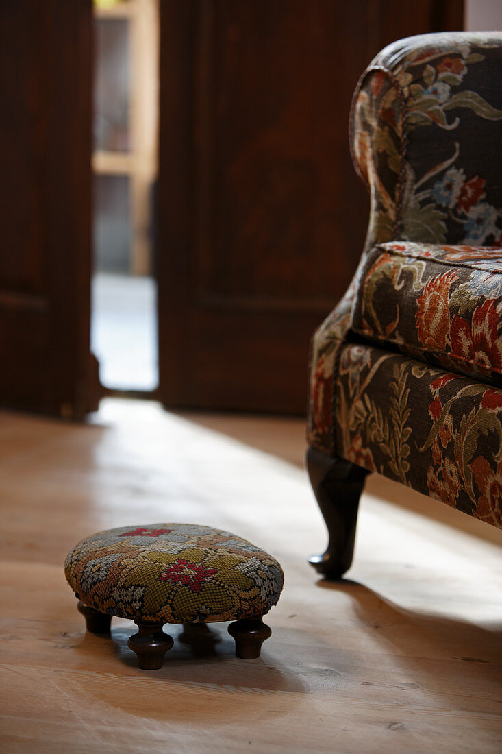 Armchair with floral upholstery and upholstered footstool in rustic setting