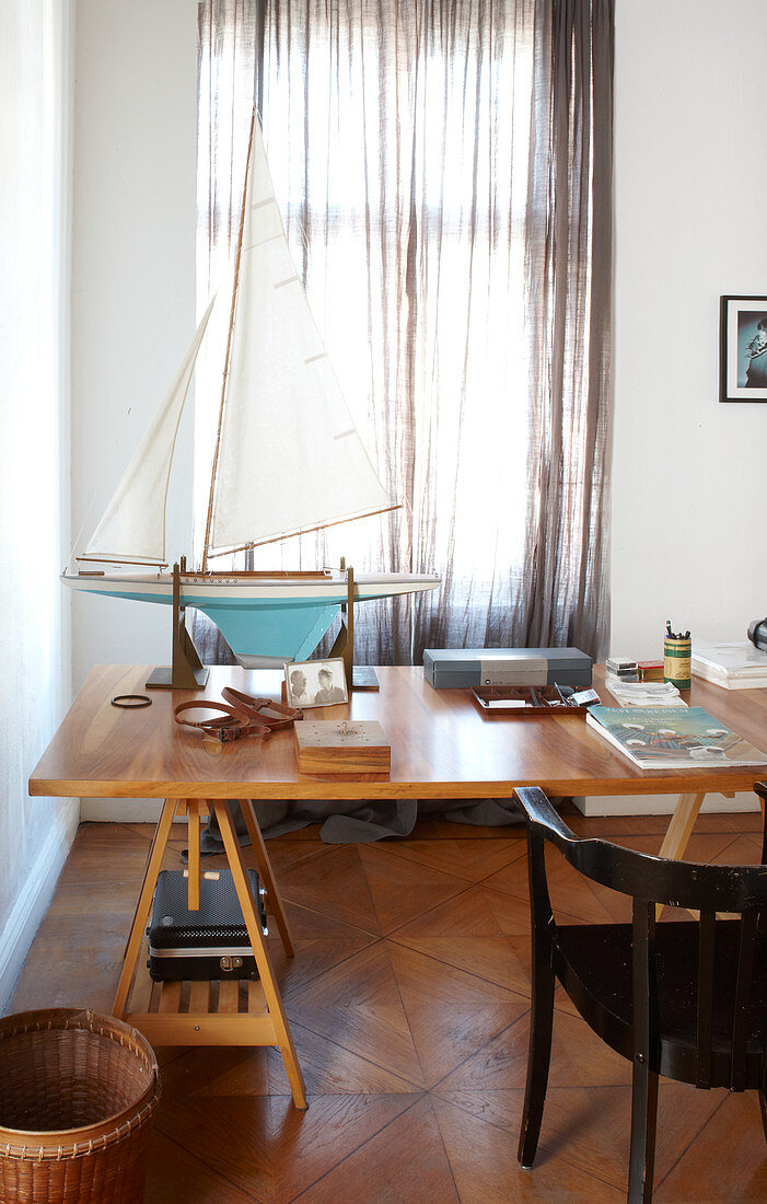 Model sailing boat on wooden table in front of window with closed, transparent curtains
