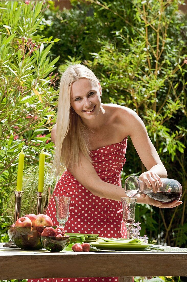 A woman pouring red wine into a glass on a garden table