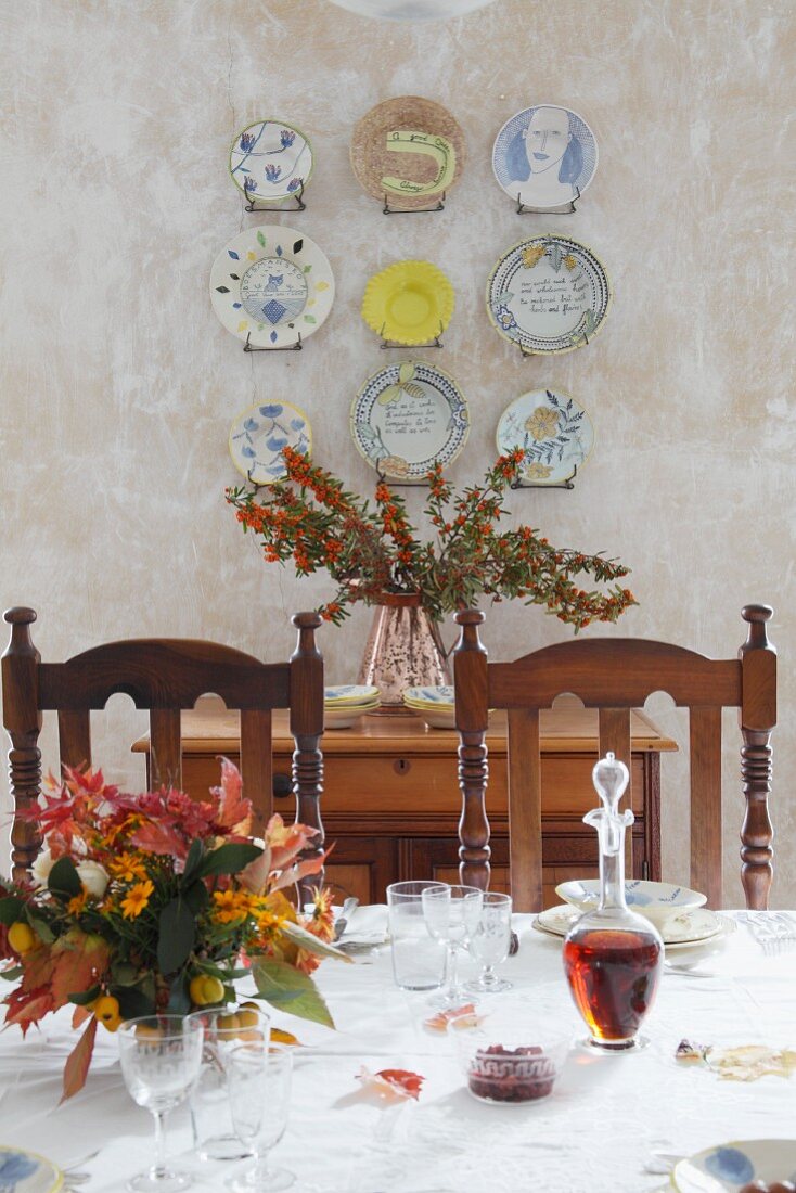 Blick über festlich gedeckten Tisch auf Wandteller an verputzter Wand aufgehängt