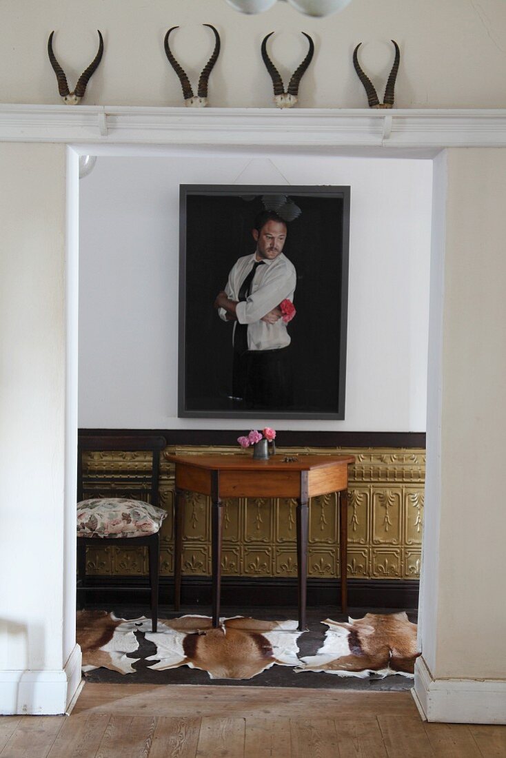 Blick durch breiten Durchgang auf Bild an Wand über Wandtisch vor halbhoher, vergoldeter Holzverkleidung und Tierfell auf Boden