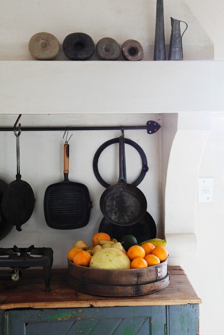 Obstbehälter auf schlichtem Unterschrank und an Wand gehängtes Vintage Kochgeschirr