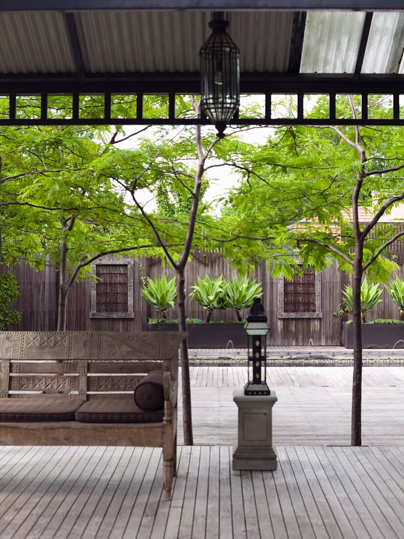 Asian bench under a covered wooden terrace with a view of an inviting green courtyard