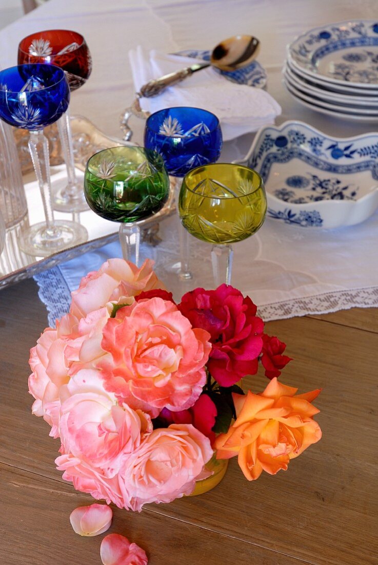 Kleiner Rosenstrauss, Bleikristallgläser und blau-weisses Geschirr auf einem Holztisch