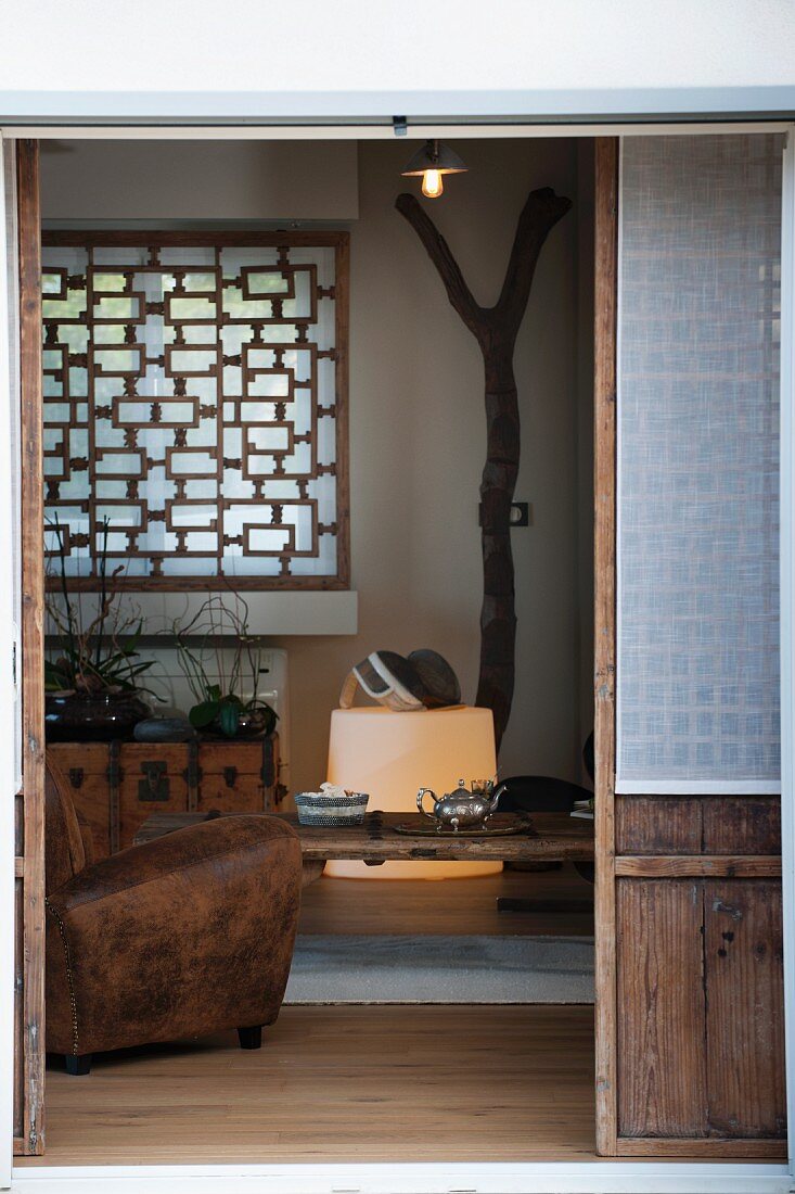 Blick durch offene Terrassentür ins Wohnzimmer auf Ledersessel und Holzgitter am Fenster