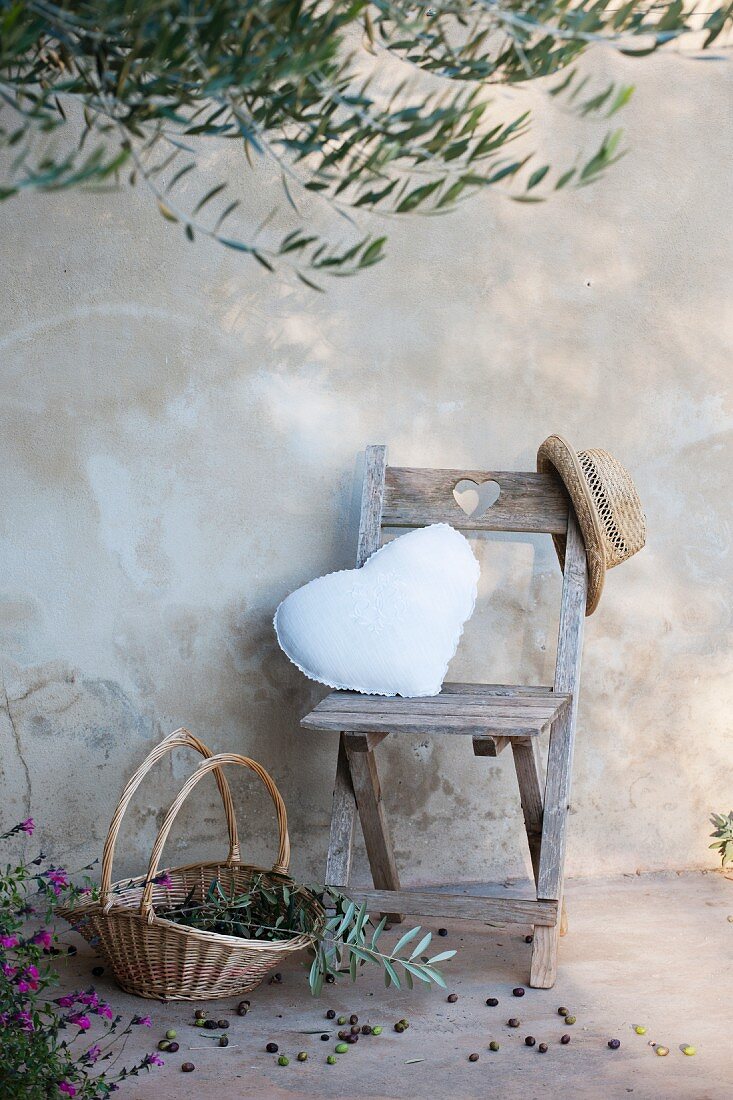 Wooden chair with heart-shaped cushion below olive tree