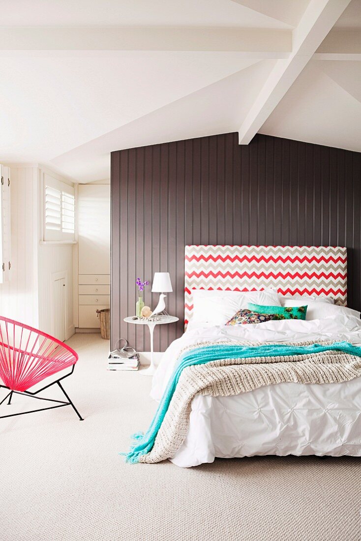 Schlafzimmer mit Doppelbett & gemustertem Kopfteil vor Trennwand aus Holz