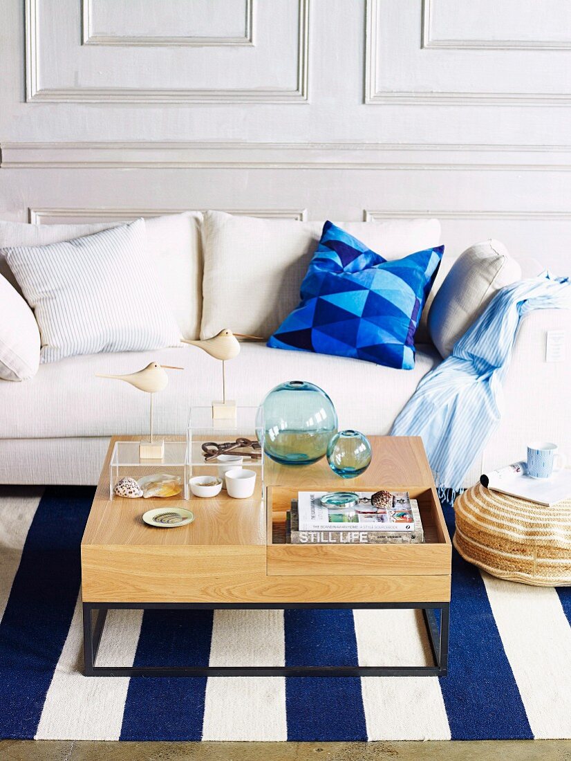 Sitzecke in Wohnzimmer mit weißem Sofa, blau-weiss gestreiftem Teppich & Couchtisch mit maritimer Deko