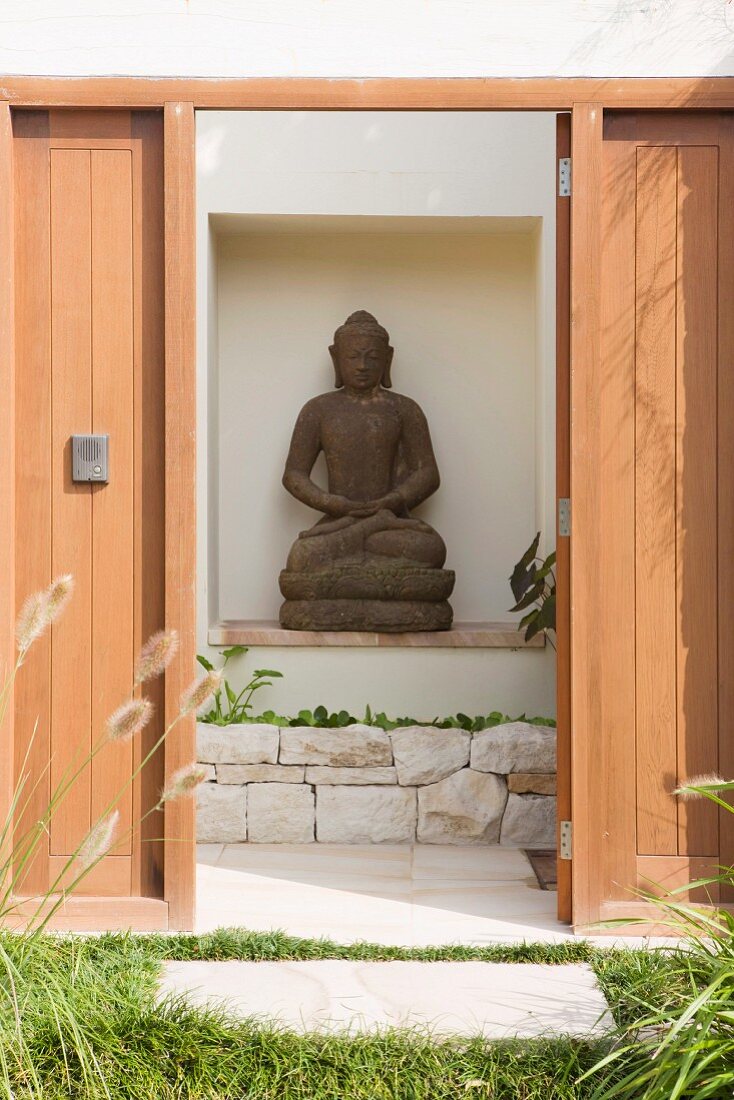 Blick durch offene Tür auf Buddhastatue in Wandnische einer Aussenmauer