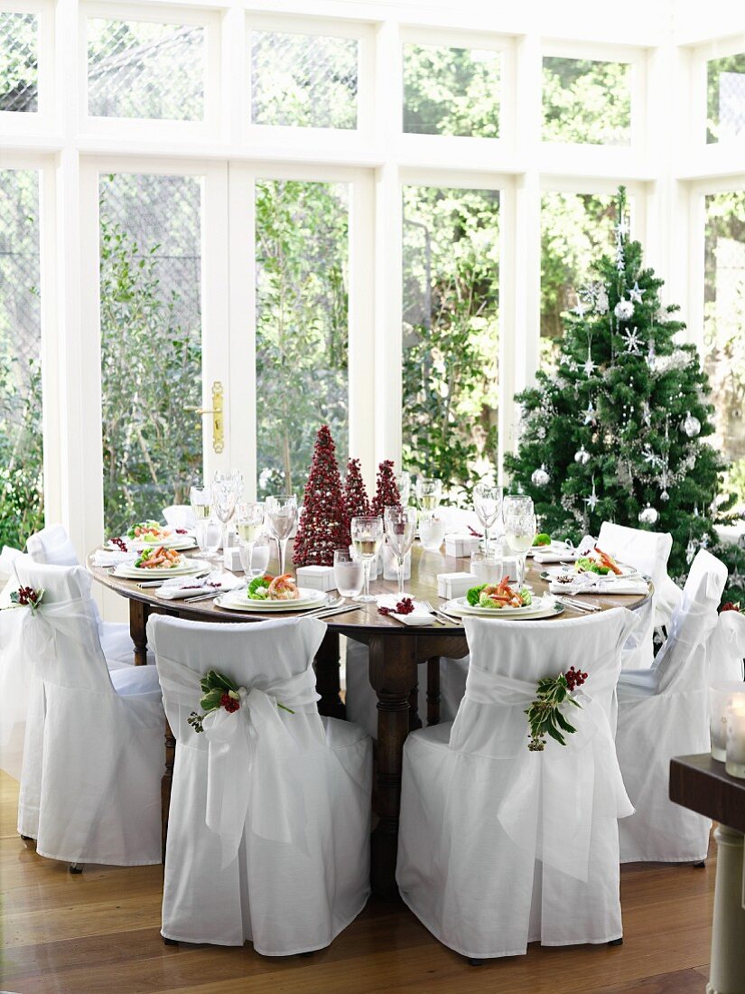 Festlich gedeckter Weihnachtstisch im Wintergarten mit Stühlen in eleganten Stoffhussen