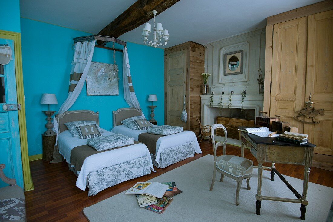 Detailed interior design in country-house bedroom - twin beds with pale, patchwork-style fabrics against wall painted light blue
