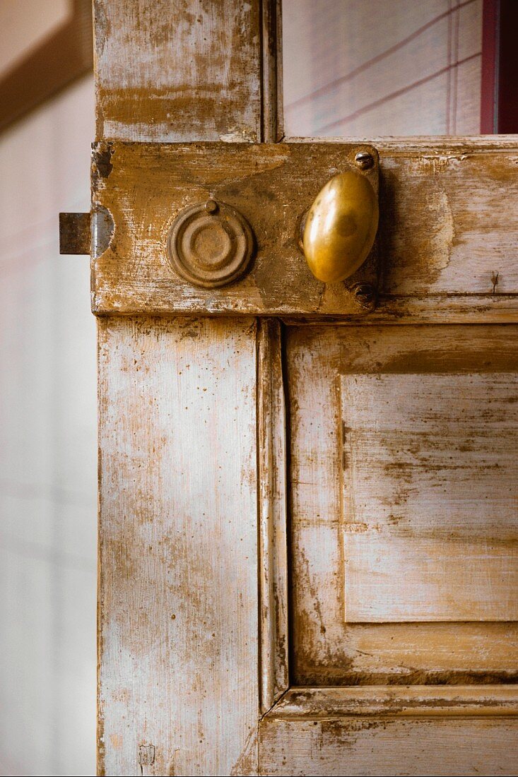Small, oval brass doorknob on old, shabby-chic interior door