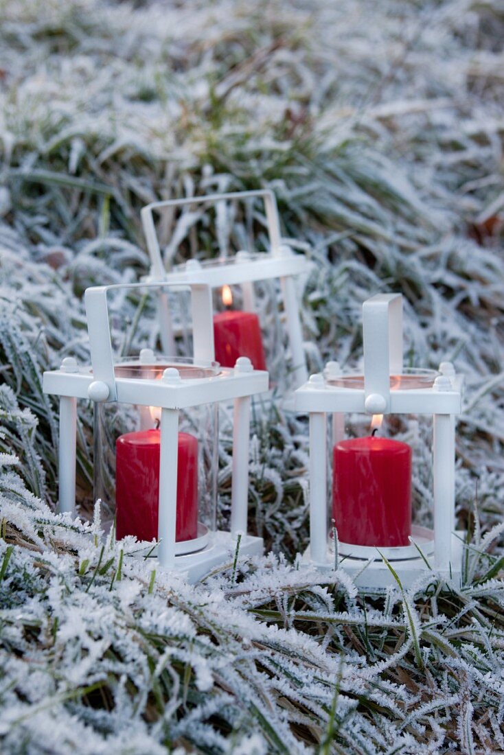 Drei weiße Metallwindlichter mit roten Kerzen