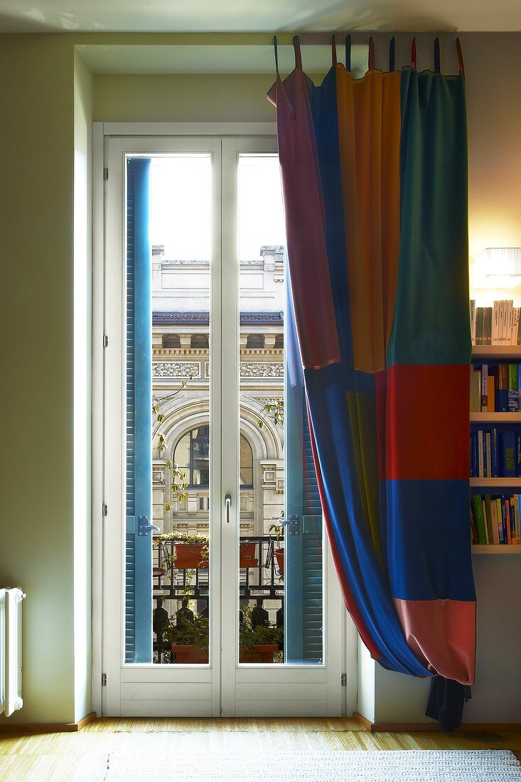 Floor-length curtain in colourful checks at balcony door with view of historic architecture
