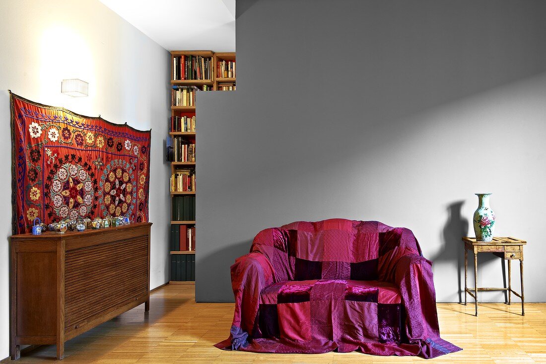 Sofa mit farbigem Überwurf vor grau getöntem Raumteiler in modernem Wohnzimmer mit traditionellem Flair
