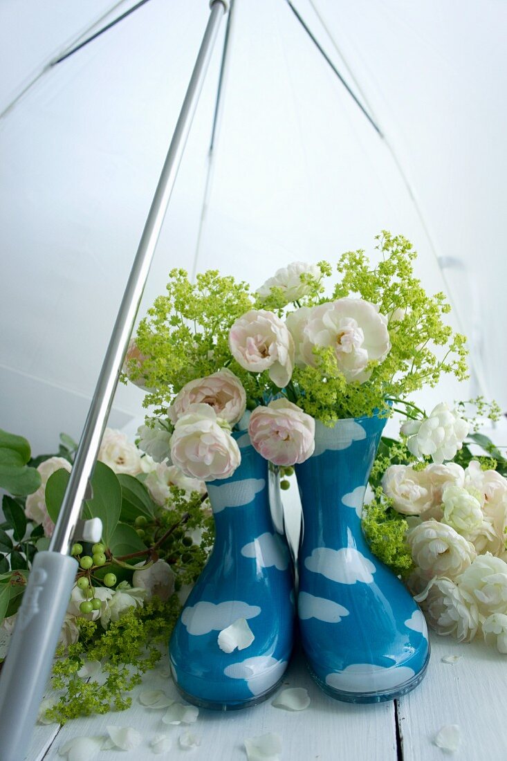 Stillleben mit Gummistiefeln & Blüten unter Regenschirm
