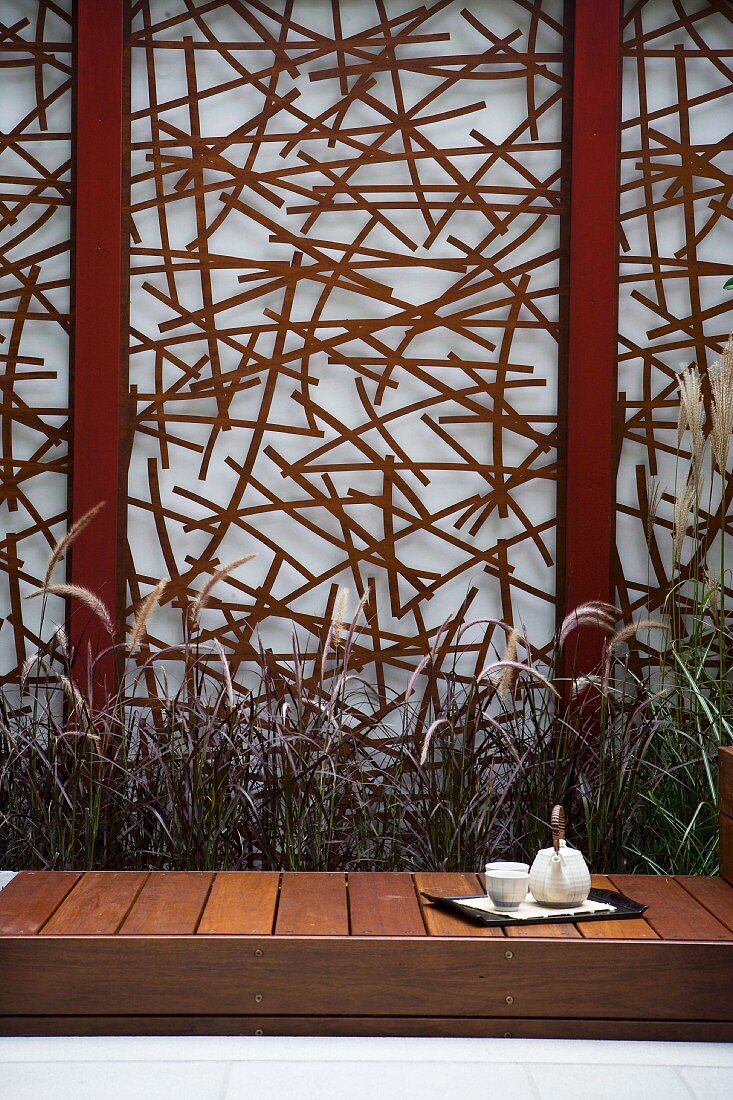 Teatime im Gartenhof - puristische Holzbank vor künstlerisch gestalteter Sichtschutzwand