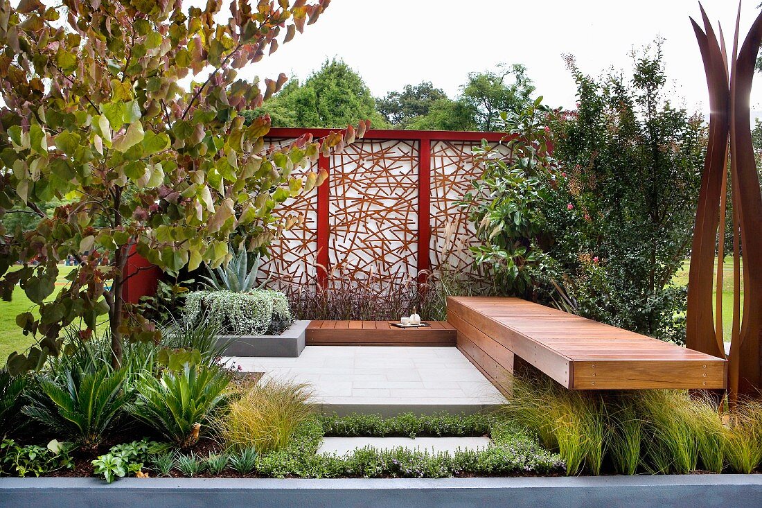 Meditativer Gartenplatz im japanischen Stil mit Holzbank und künstlerisch gestalteter Sichtschutzwand