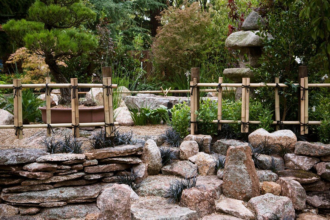 Japanischer Steingarten mit verschnürten Bambus-Zäunen und Steinlampe im Hintergrund