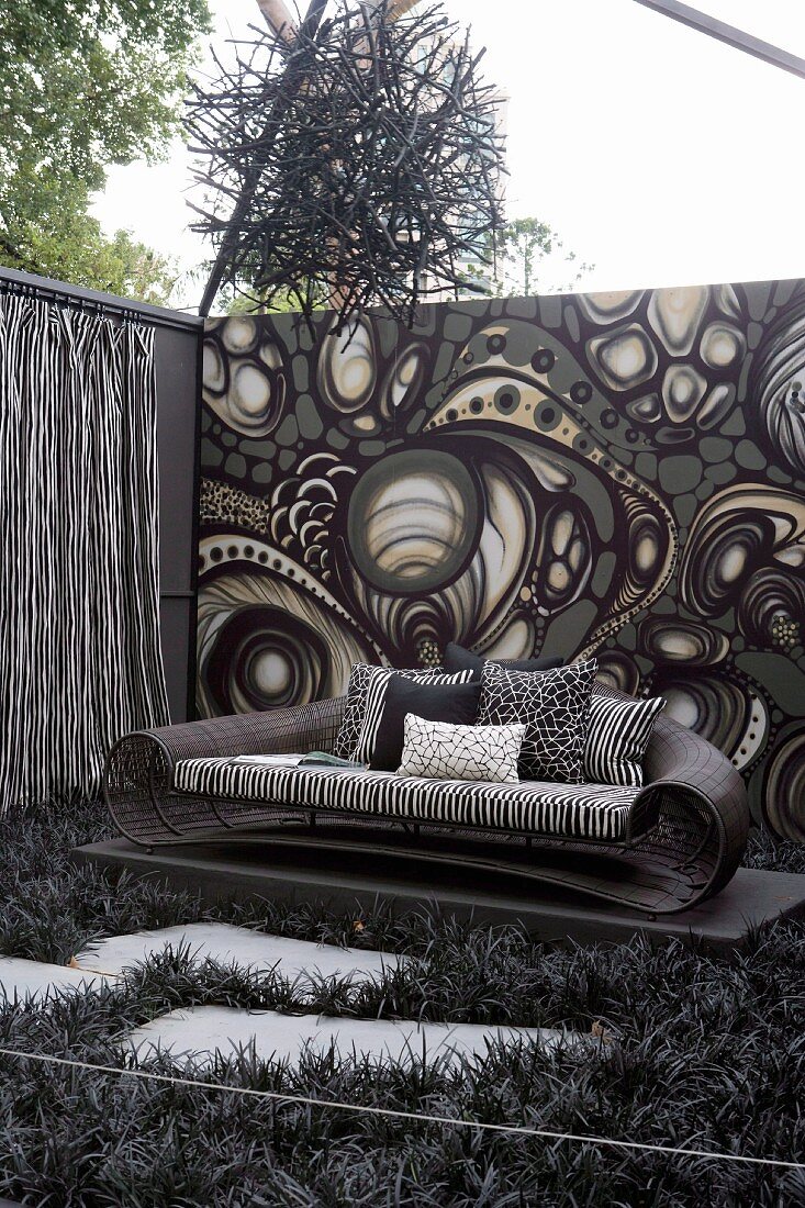 Expansive wicker sofa against back wall with psychedelic black and white pattern below suspended artwork made from twigs