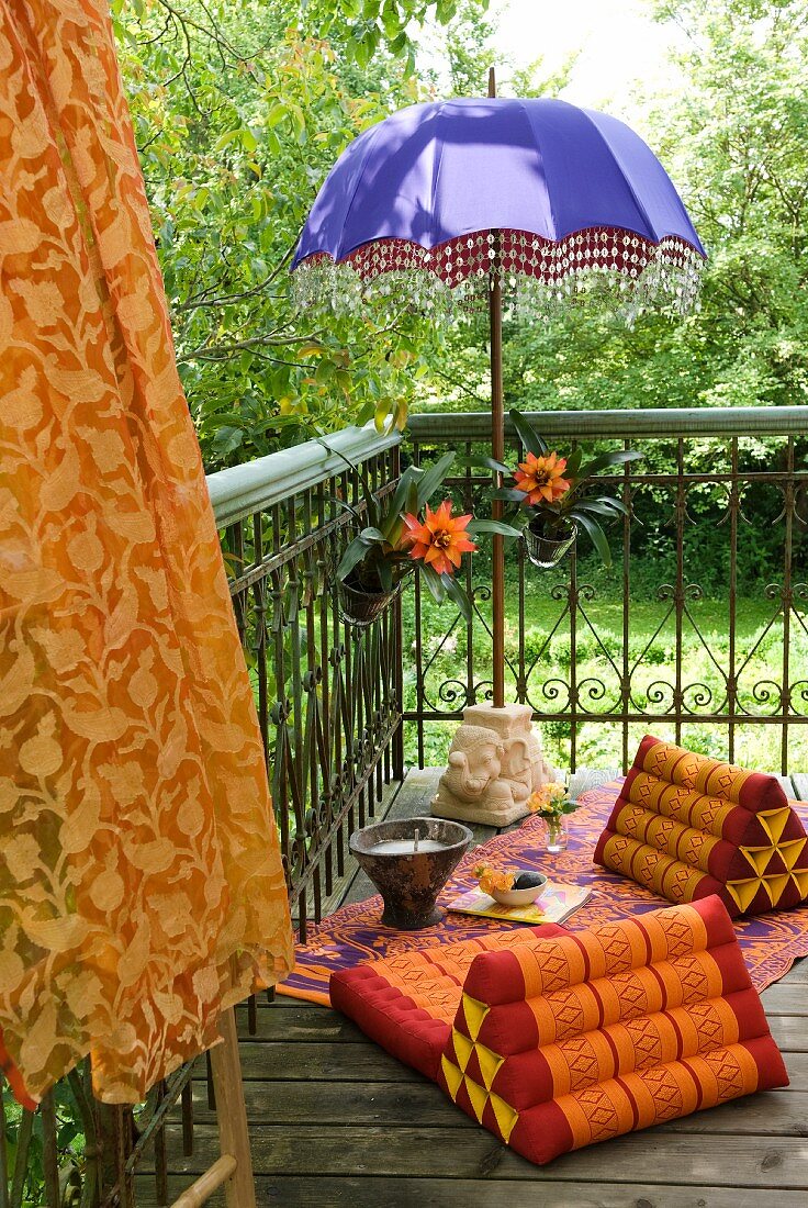 Blauer Schirm mit Perlenfransen und Rückenkissen auf einer bunten Decke als exotischer Sitzplatz auf dem Balkon