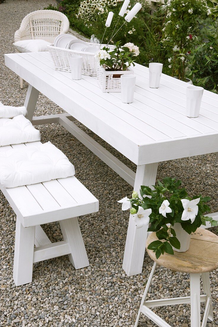 Weisser Gartentisch und passende Sitzbank mit Blumendeko und Porzellangeschirr