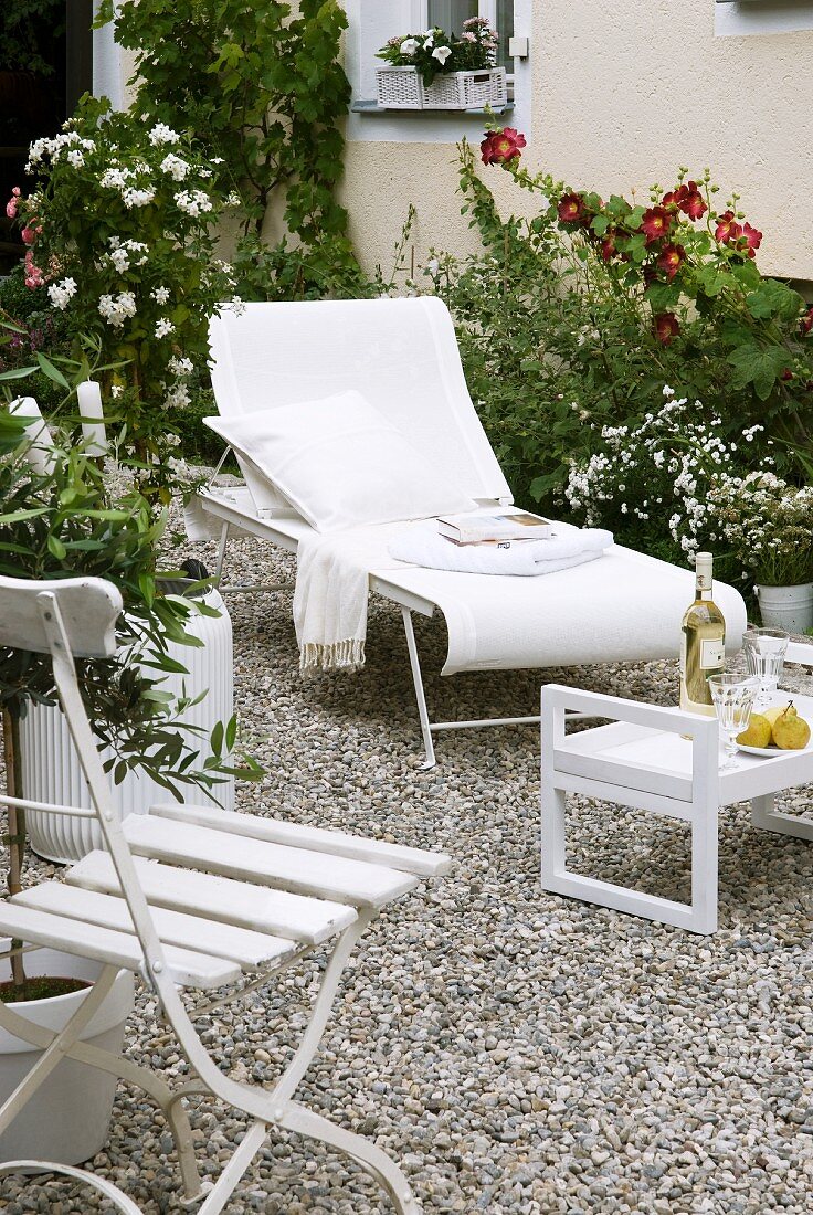 White sun lounger, folding chair and tray table on gravel surface in garden
