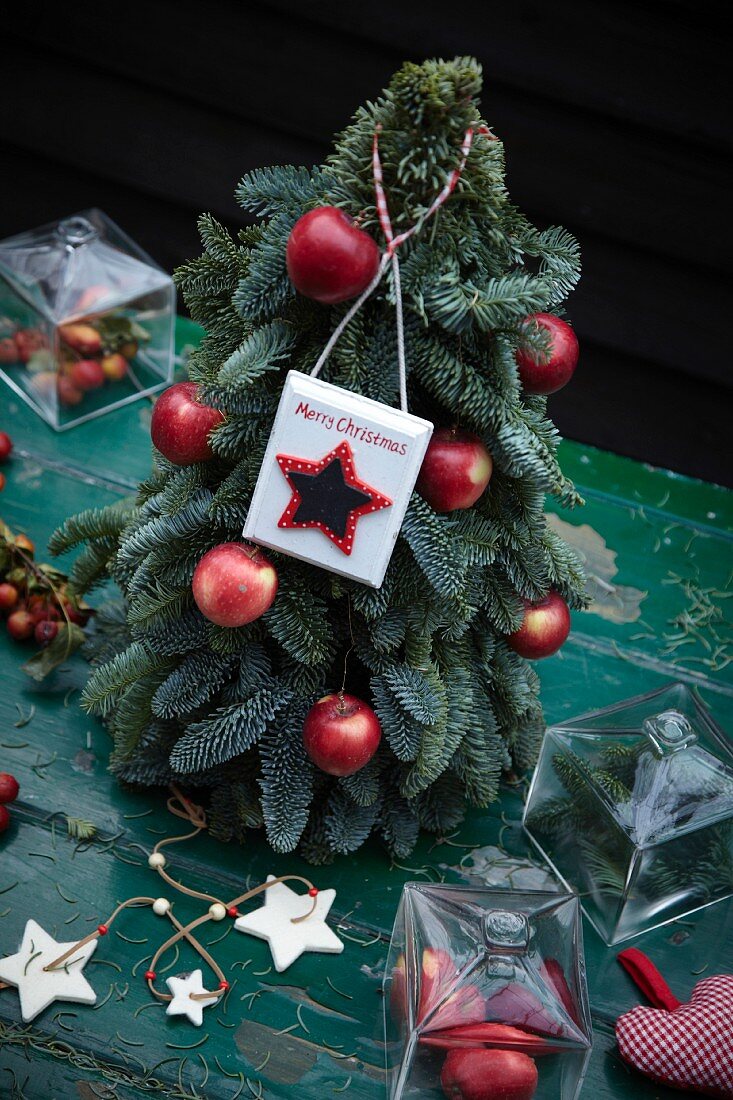 Christbaum mit roten Äpfeln und Schild Merry Christmas
