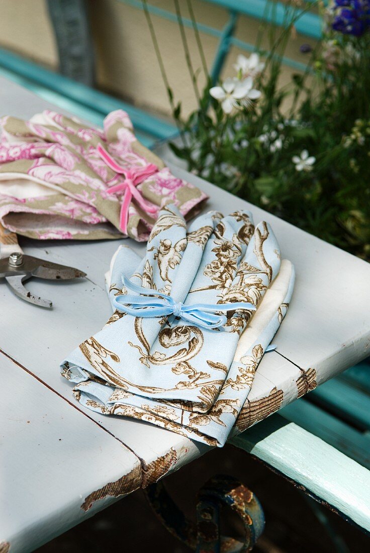 Feminine Gartenhandschuhe in Rosa und Hellblau mit klassischem französischen Dessin auf einem alten Gartentisch
