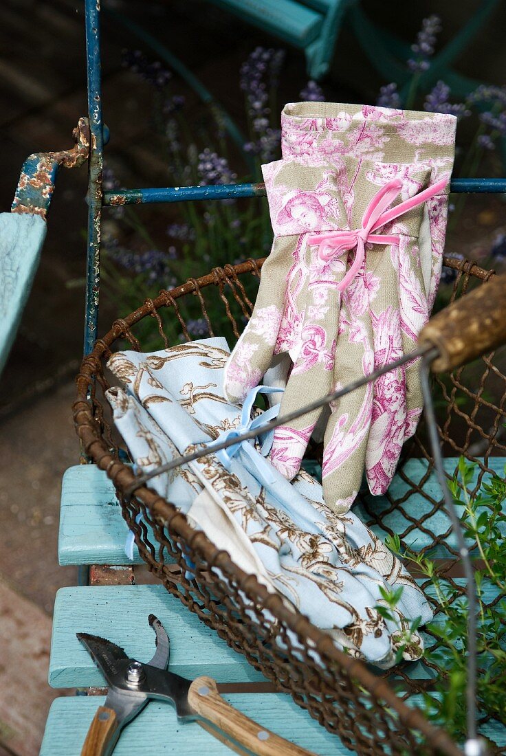 Makellose Gartenhandschuhe mit femininem, französischen Dessin in altem Drahtkorb auf einem Gartenstuhl